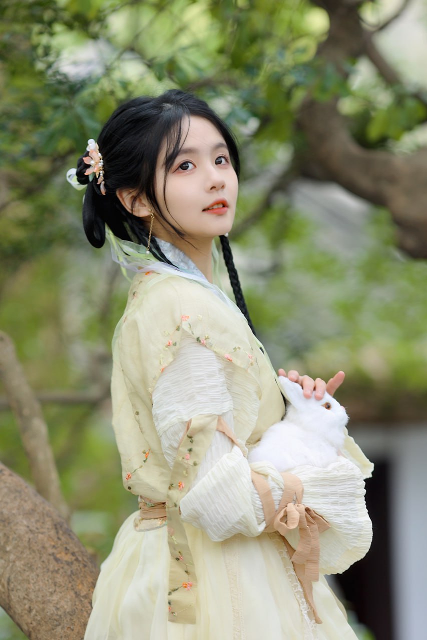 女子怀抱白兔，站在树下，眼神清澈