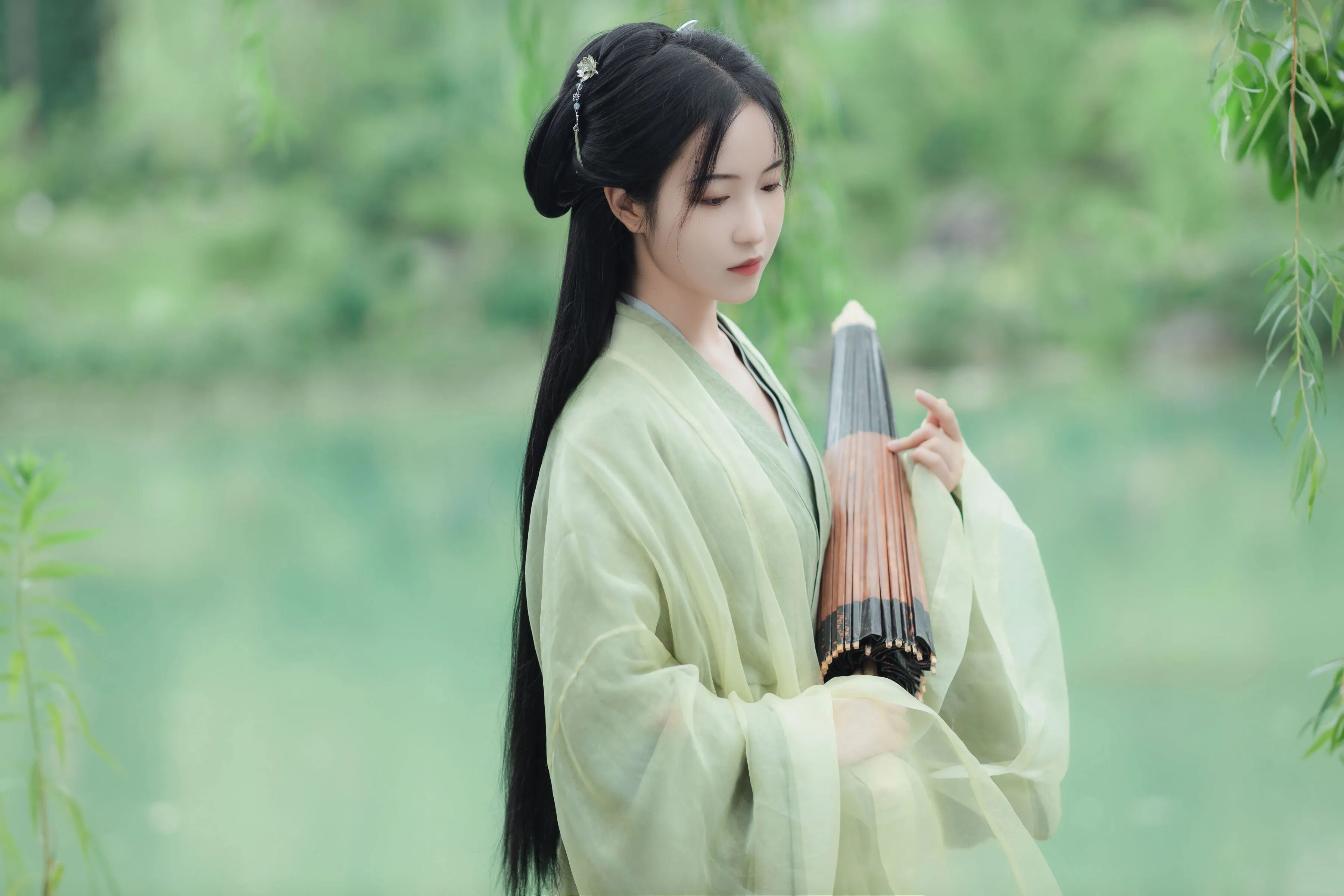 侧身持伞立于湖边柳下