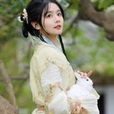 女子怀抱白兔，站在树下，眼神清澈